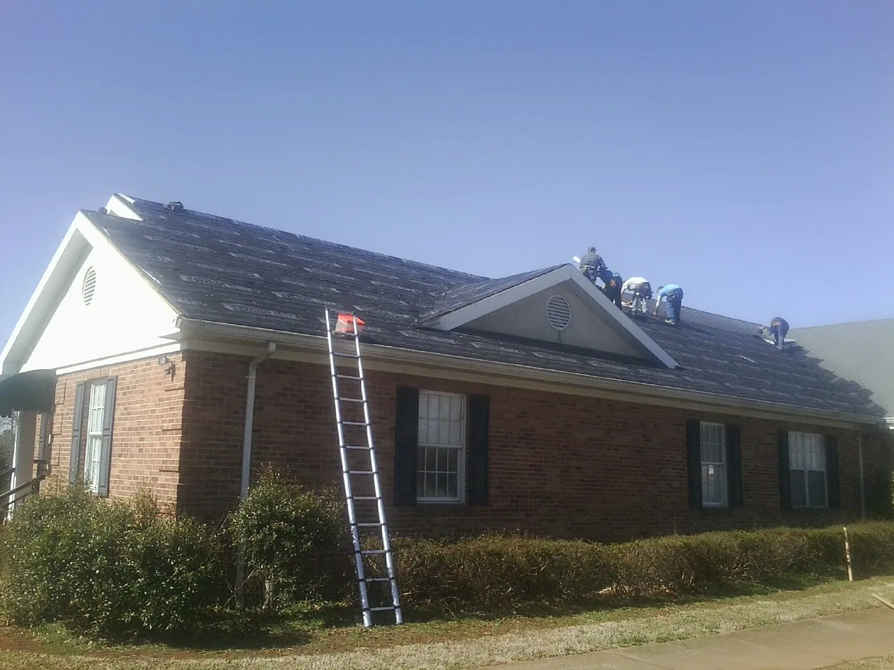 Crew tearing shingles off a brick ranch roof with a ladder set — Emergency Roof Repair work by our crew in Cannon Beach