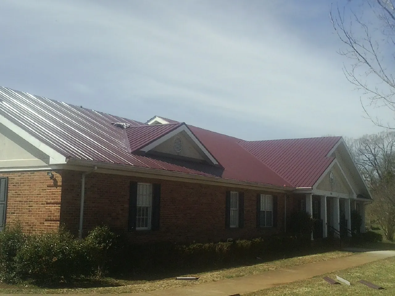 Red metal roof with gabled entries on a long brick building, from a Hail Damage Roof Repair job in Cannon Beach