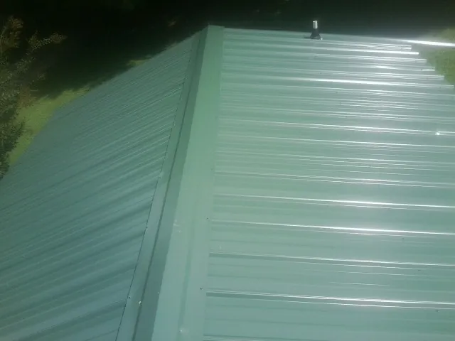 New green metal panels meeting at the ridge of a roof — Flat Roof Repair work by our crew in Cannon Beach
