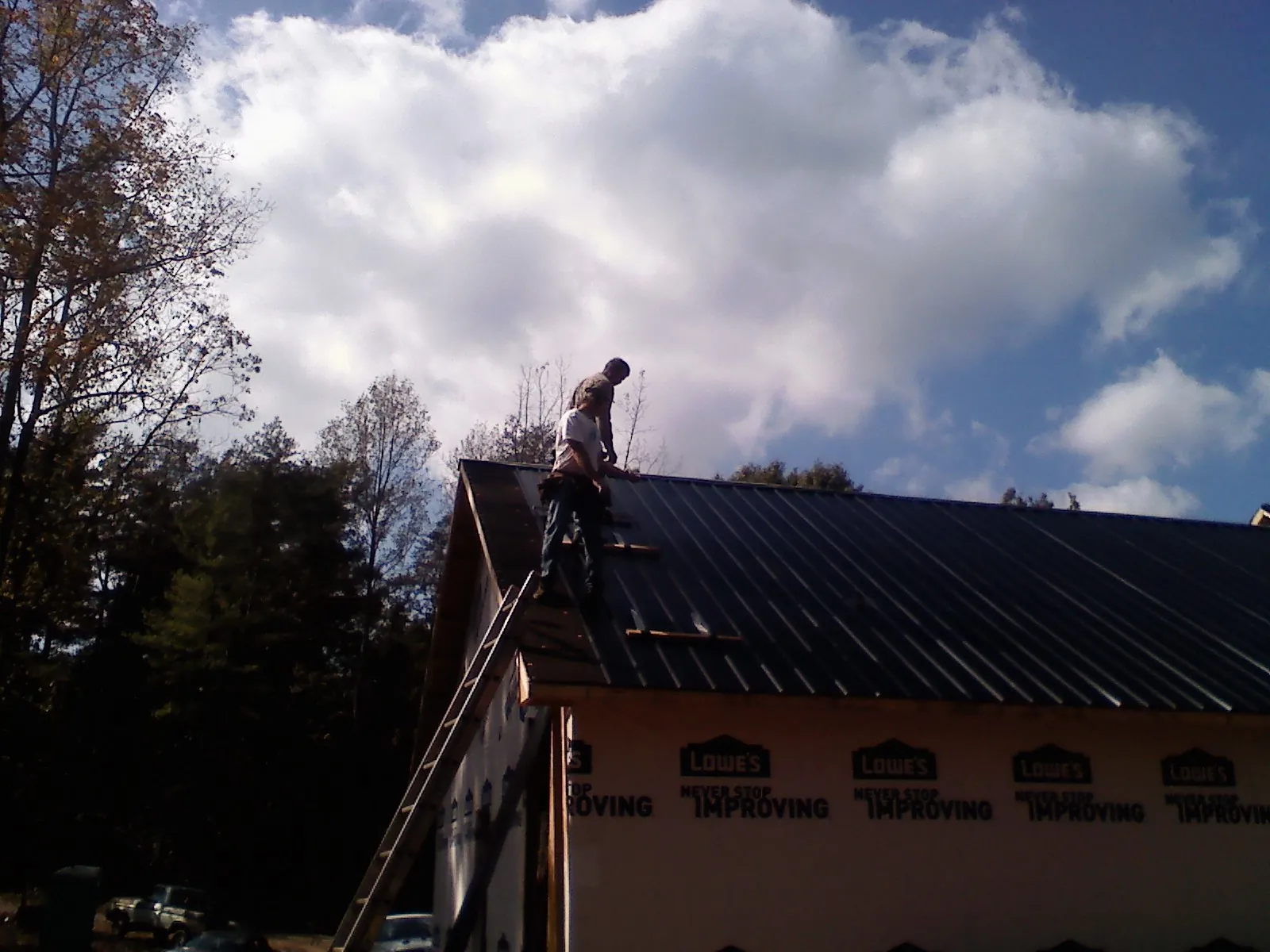 Roofer fastening dark metal panels high against a cloudy sky, from a Roof Inspection job in Cannon Beach