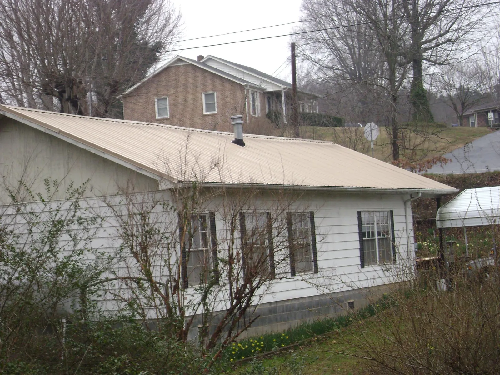 Tan metal roof on a white sided house set into a hillside — Commercial Roofing by Roofing Brothers in Cannon Beach