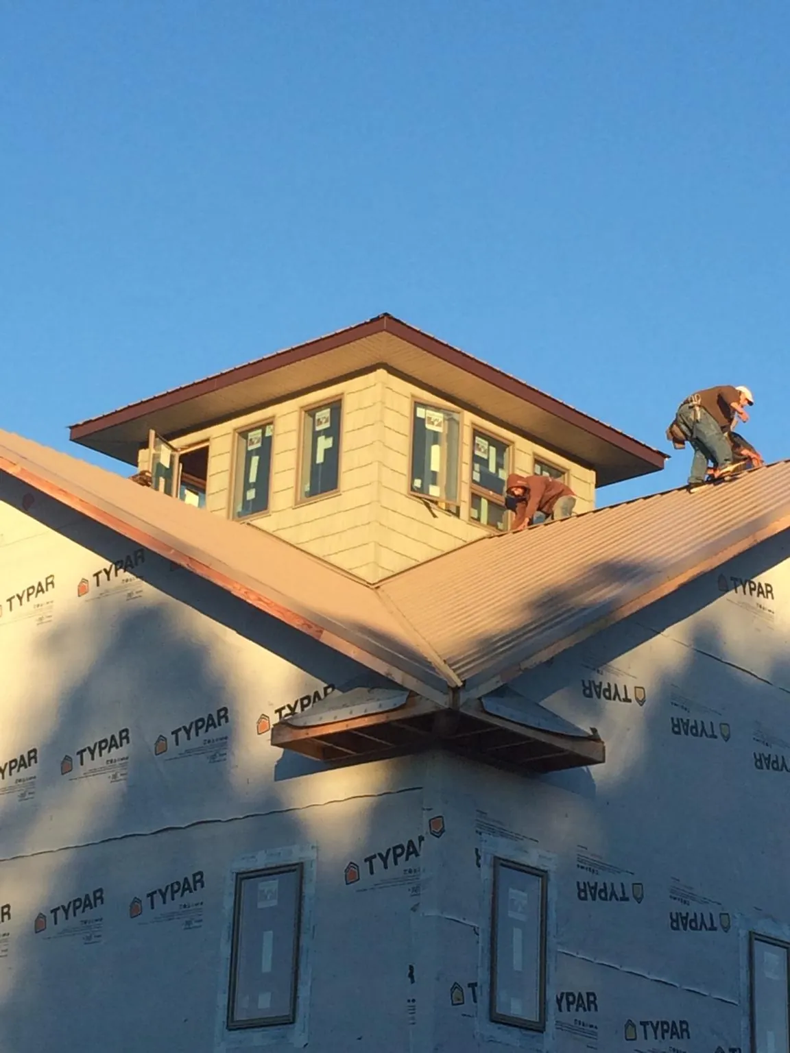 Roofers working around a rooftop cupola on a new metal roof at sunset — Roof Waterproofing in Cannon Beach by Roofing Brothers